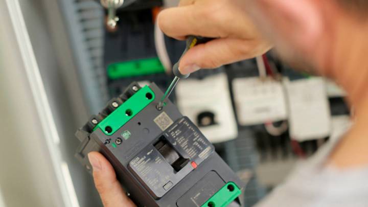 Technician installing a Schneider Electric molded-case circuit breaker in a control panel